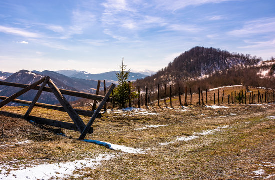 broken wooden fence on hillside. springtime is coming. beautiful mountainous landscape with some snow on slopes with weathered grass on a bright day