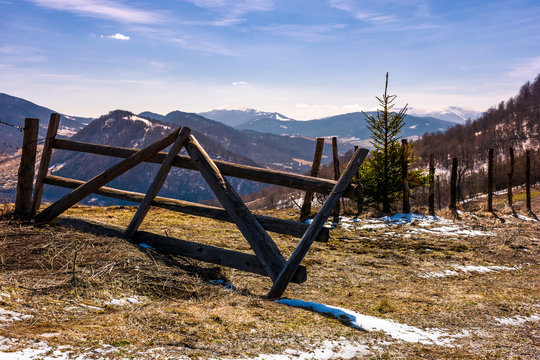 broken wooden fence on hillside. springtime is coming. beautiful mountainous landscape with some snow on slopes with weathered grass on a bright day