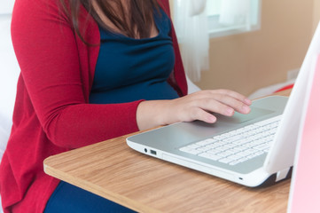 Fototapeta premium Asian pregnant woman wearing red cardigan using laptop and credit card for shopping online website on wooden table and many shopping bag