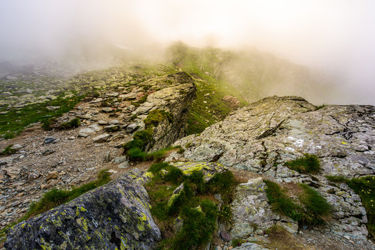 rocky cliffs of Fagaras mountains in fog. fantastic atmosphere of mysterious scenery of Romania Carpathians in summer. sun is shining behind the haze.