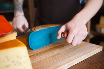 Cutting gouda pesto blue cheese in grocery shop