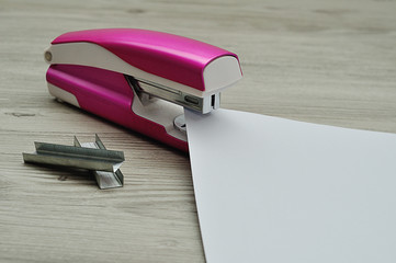 A pink stapler with papers and a pile of staplers on a table