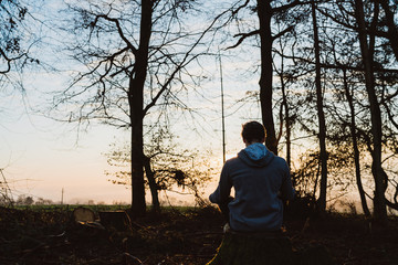 Young man meditating at sunrise in a forrest in Austria