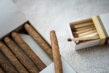 Cigars and whiskey on a light table cloth, one cigar out of the packet