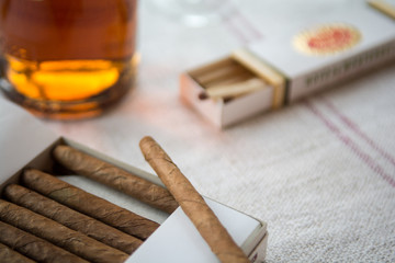 Cigars and whiskey on a light table cloth, one cigar out of the packet