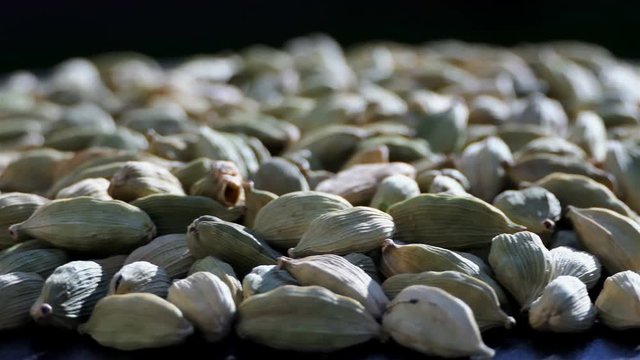 green cardamom seeds rotating in slow motion over black background 4k. Macro Pile of cardamom rotation with copy space. Heap of Cardamom in the nature with sun light. Aromatics and spices background.