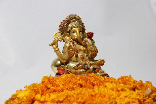 Ganesha made from brass with foreground yellow marigold flower and white background, the son of Uma Devi god in Hinduism and Brahmanism. God of knowledge and arts.