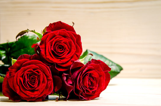 Three beautiful red roses lie on a wooden surface.
