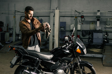 Young man in leather jacket standing near motorcycle in garage