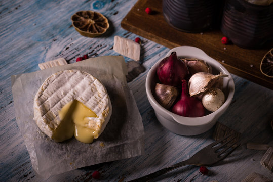 Hot camembert cheese on wooden board with garlic and onion