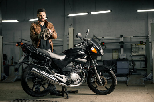 Fototapeta Young man in leather jacket standing near motorcycle in garage