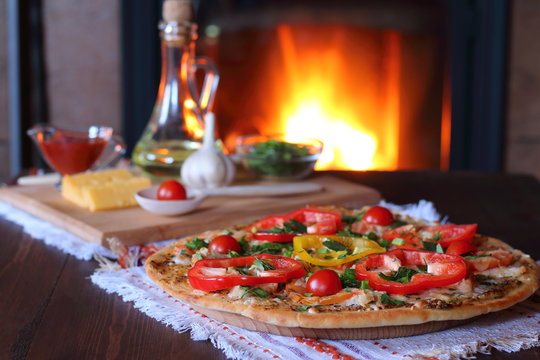 Cooked pizza, vegetables and ingredients are on the table on the background of fire from the oven.