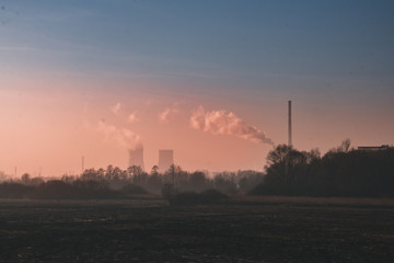 Fototapeta na wymiar Landscape with field and trees, in the distance factory and a power station, with the factory pipes going smoke against the red sky, Severe pollution of the environment