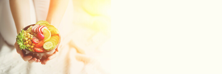 Girl in white jeans holds in hands fork, vegan breakfast meal in bowl with avocado, quinoa, cucumber, radish, salad, lemon, cherry tomatoes, chickpea, chia seeds. Top view, copy space. Banner