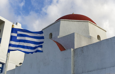 Mykonos, Greece Greek flag by whitewashed church. Day view of Greek flag waving in the wind by an orthodox church at Mykonos Town waterfront. © bestravelvideo