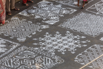 Unidentified indian woman seen drawing kolam (in tamil language) or rangoli using white colored rice during festival season