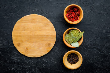 Mock up for menu or recipe. Wooden cutting board near bowls with goji, bay leaf, pepper on black background top view