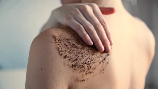 Beauty, spa and healthy skin concept - woman cleans skin of the body with coffee scrub in bathroom.