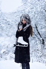Fototapeta na wymiar Girl with pair of figure skates at trees in snow