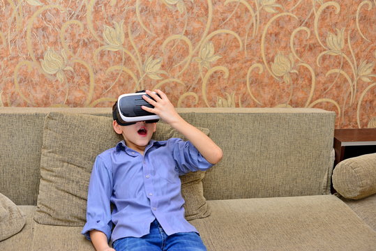 Happy teen boy wearing virtual reality goggles watching movies or playing video games. Cheerful smiling looking in VR glasses and making thumb up gesture. Child experiencing virtual reality.