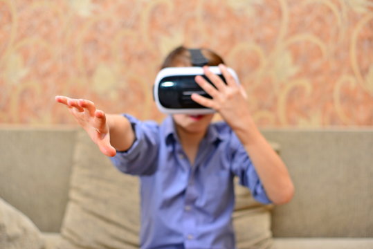 Happy teen boy wearing virtual reality goggles watching movies or playing video games. Cheerful smiling looking in VR glasses and making thumb up gesture. Child experiencing virtual reality.