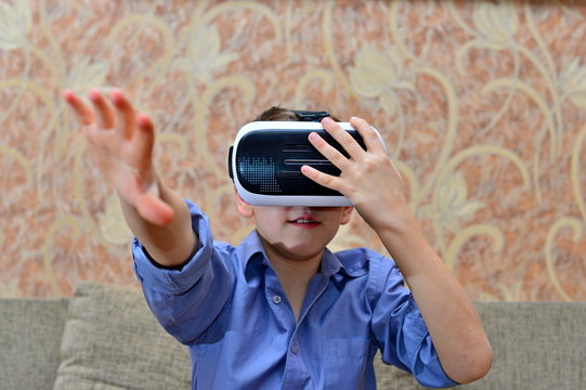 Happy teen boy wearing virtual reality goggles watching movies or playing video games. Cheerful smiling looking in VR glasses and making thumb up gesture. Child experiencing virtual reality.
