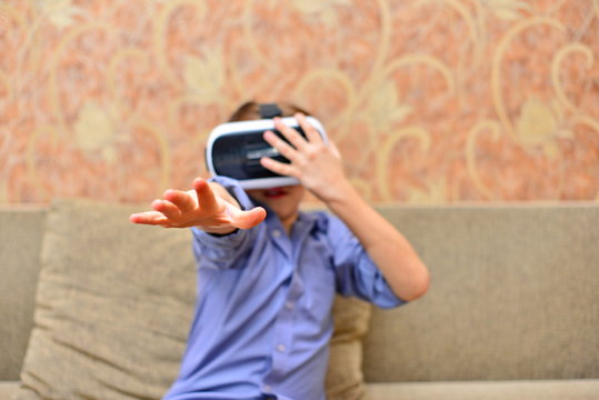 Happy teen boy wearing virtual reality goggles watching movies or playing video games. Cheerful smiling looking in VR glasses and making thumb up gesture. Child experiencing virtual reality.