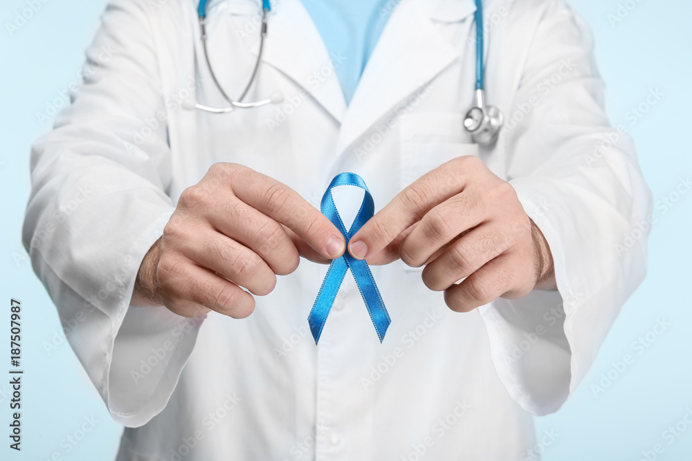 Sticker Doctor holding blue ribbon on color background. Cancer awareness concept