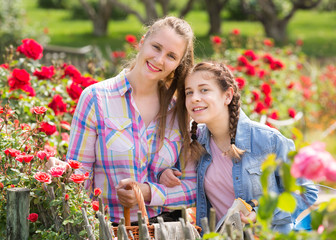 woman and  girl holding a basket and standing near  blooming roses