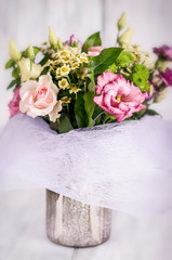 Festive bouquet of various flowers in a vase on a white wooden background