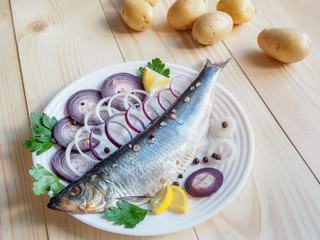 Appetizing salted herring fillet with onion, lemon and spices on the plate.
