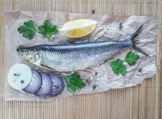 Appetizing salted herring fillet with onion, lemon and spices on parchment.

