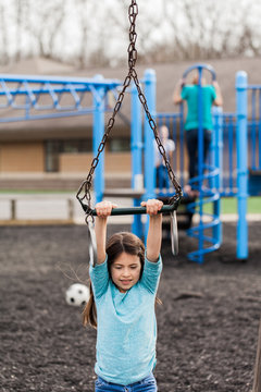 Girl swinging from a trapeze bar at school playground