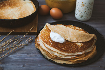 Pancakes in a skillet and ingredients for them on a wooden table