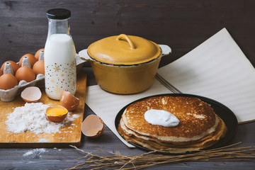 fresh, hot pancakes in a frying pan, eggs, milk, flour on a wooden table