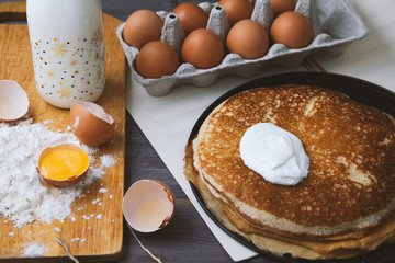 fresh, hot pancakes in a frying pan, eggs, milk, flour on a wooden table. Top view
