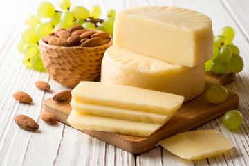 Pieces of cheese on wooden board with almonds and green grape on white wooden background.