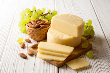 Pieces of cheese on wooden board with almonds and green grape on white wooden background.