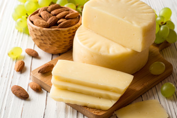 Pieces of cheese on wooden board with almonds and green grape on white wooden background.