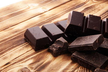 Dark brown chocolate pieces, stacks culinary wooden background.