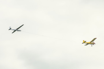 Yellow small light-engine sport plane flying in the sky pulls on a rope the glider plane