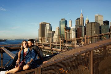 Beautiful young man and woman pose on the Brooklyn Bridge in the rays of morning sun