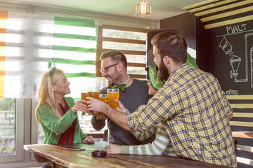 Four friends celebrate St Patrick day in pub  and dring a beer and smile