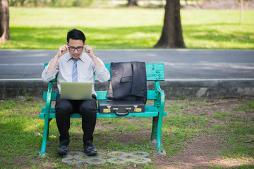 businessman sitting on bench in park relax and using tablet checking his business