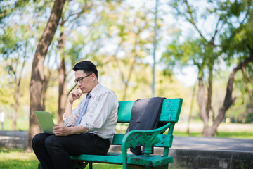 businessman sitting on bench in park relax and using tablet checking his business