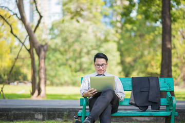 happy businessman sitting on bench in park relax and using tablet checking his business