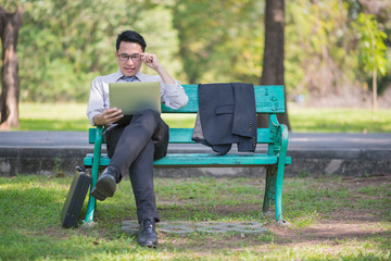 businessman sitting on bench in park relax and using tablet checking his business
