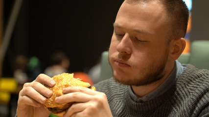 young hipster guy eating burger sitting in cafe