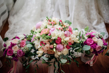 Three pink wedding bouquets stand on the floor before bride's dress