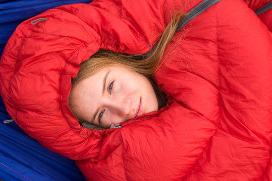 Young woman smiling while resting in in red sleeping bag